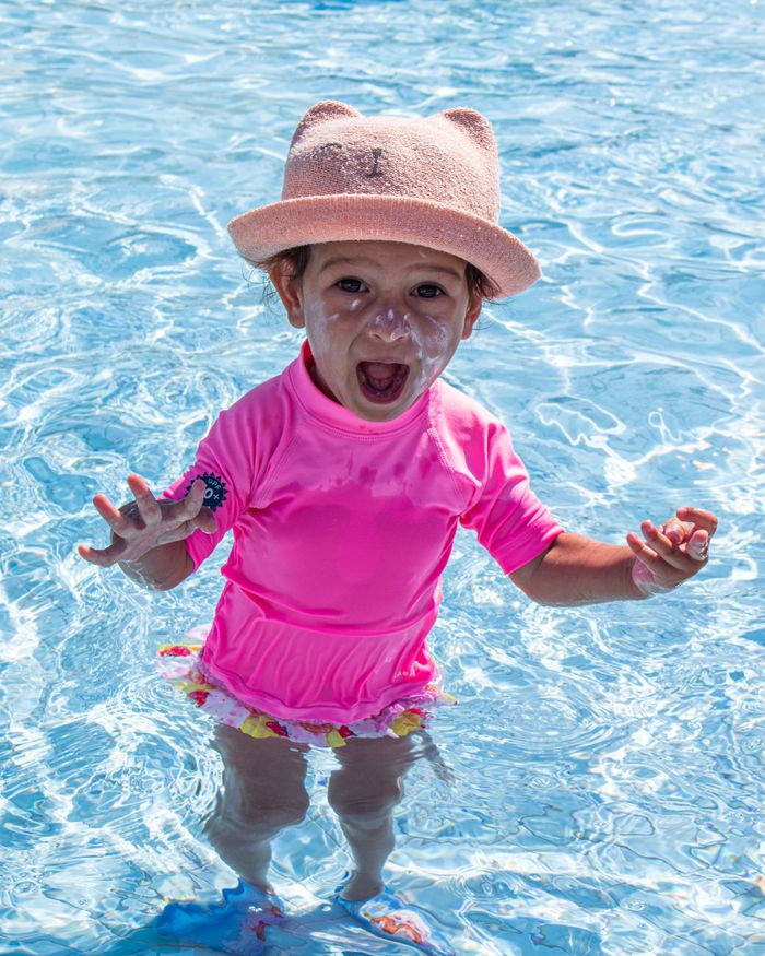 Happy child in a pink swimsuit and hat enjoying a sunny day in a swimming pool.