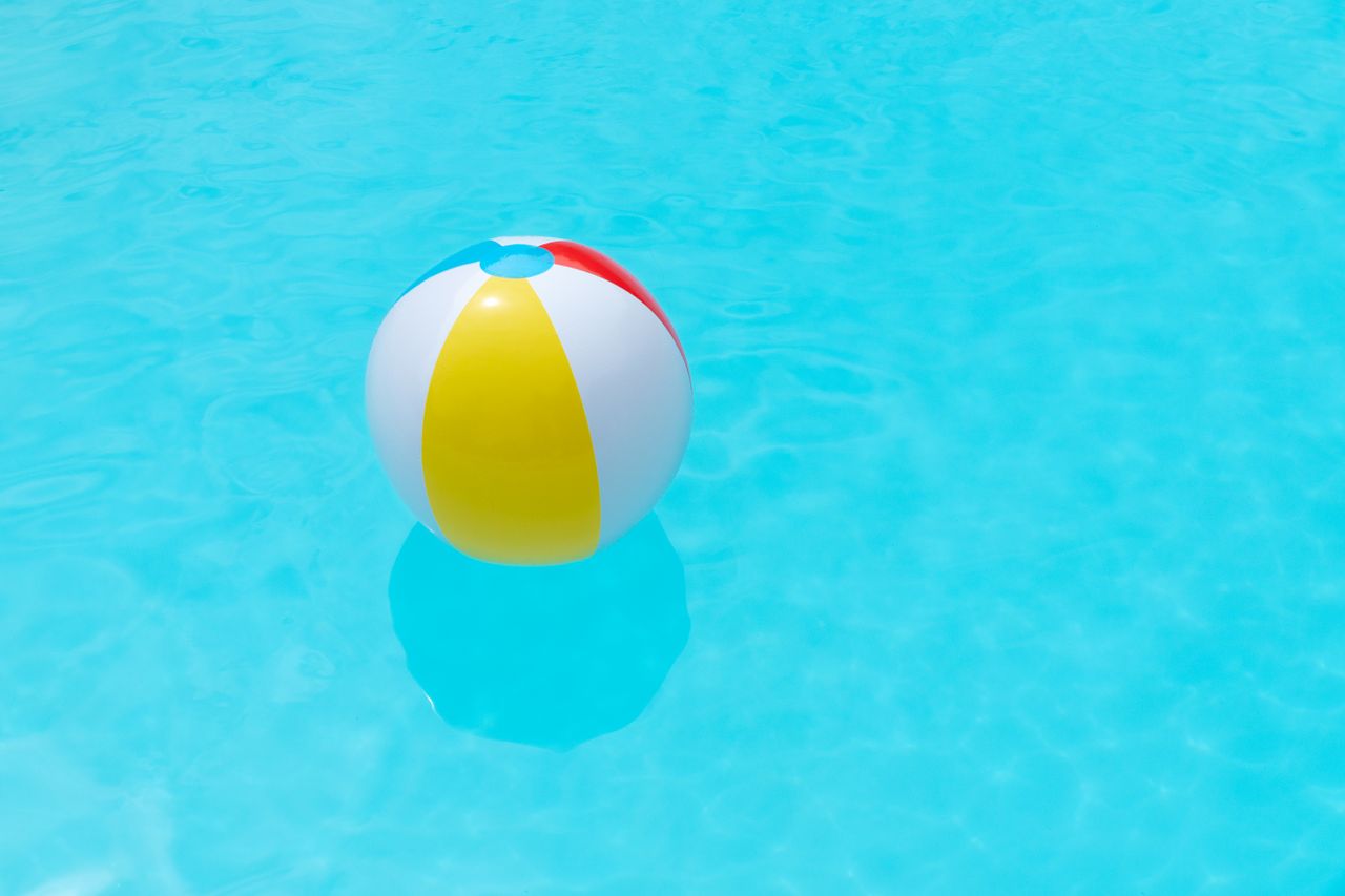Vibrant beach ball floating in a clear turquoise swimming pool, perfect for summer themes.