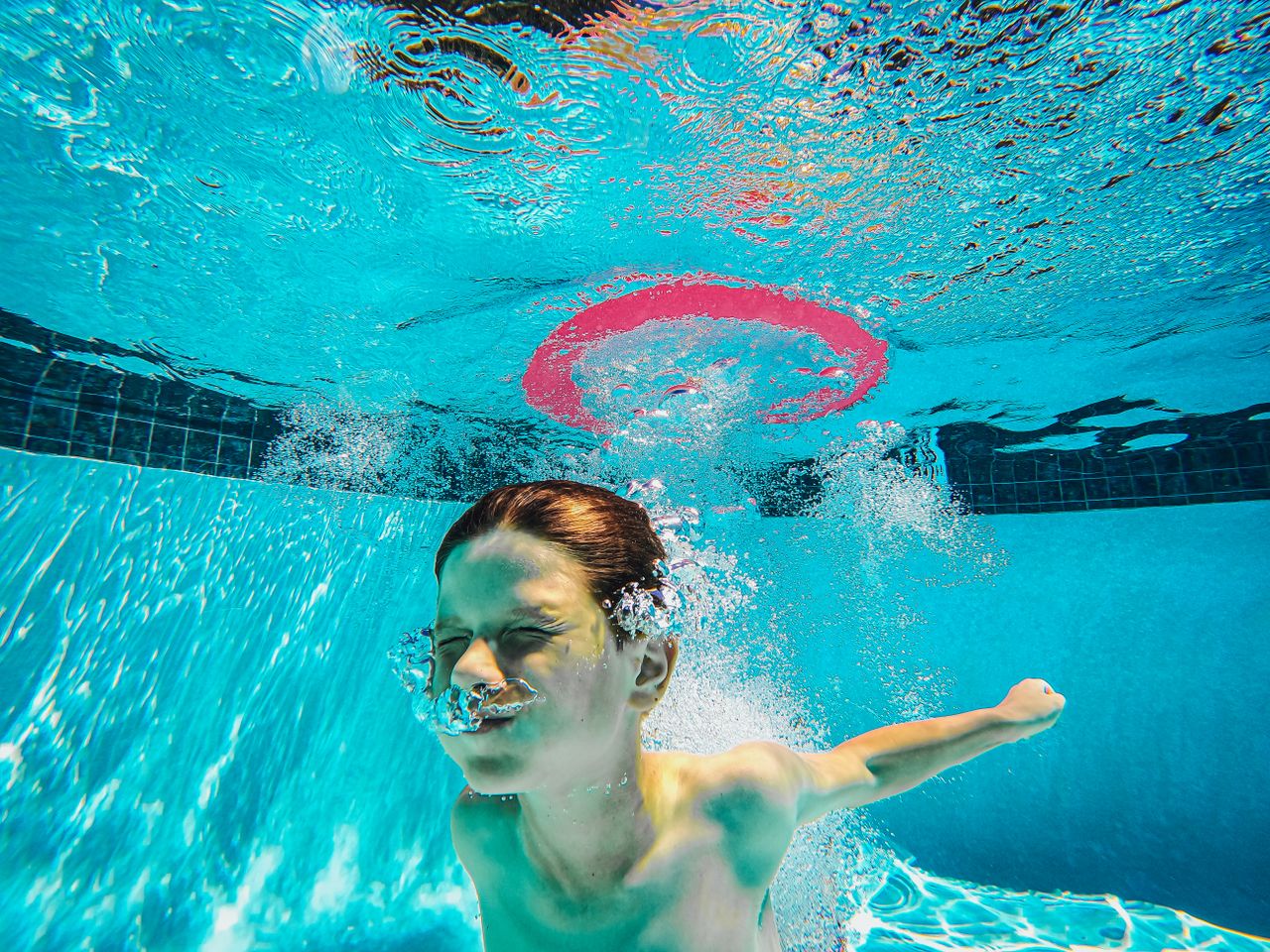 A child energetically plays underwater in a swimming pool, surrounded by bubbles and splashes.
